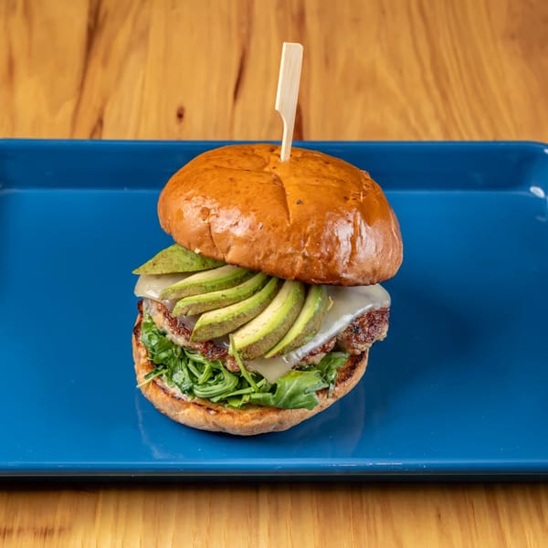 LSA Burger Co. burger with avocado, cheese, and arugula on a blue plate.
