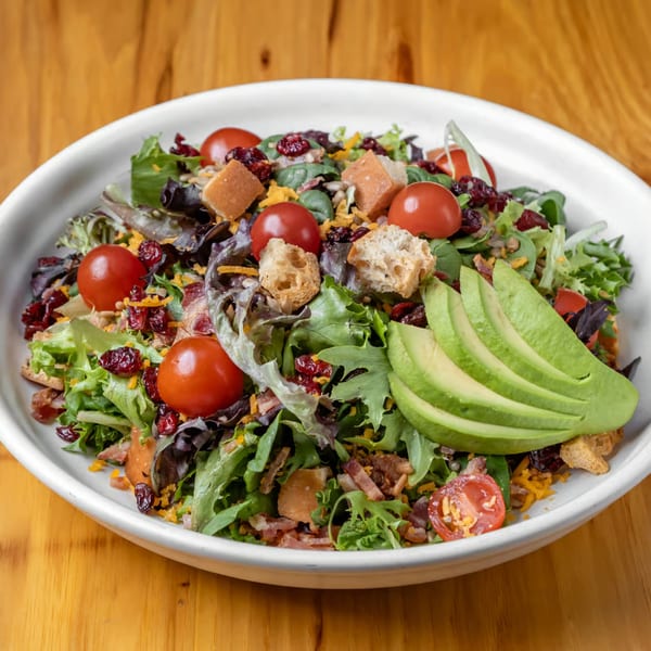 Fresh salad with mixed greens, cherry tomatoes, avocado slices, croutons, and dried cranberries.