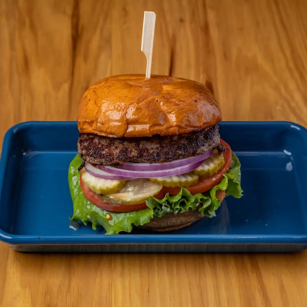LSA Burger Co. burger with lettuce, tomato, pickles, and red onion on a blue tray.