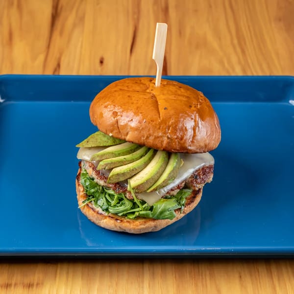 LSA Burger Co. burger with avocado, cheese, and arugula on a blue plate.