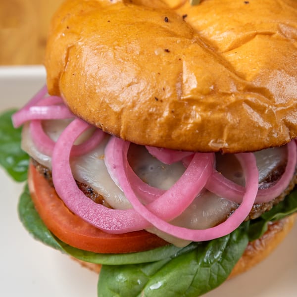 LSA Burger Co. burger with a golden bun, melted cheese, pickled red onions, tomato, and spinach.