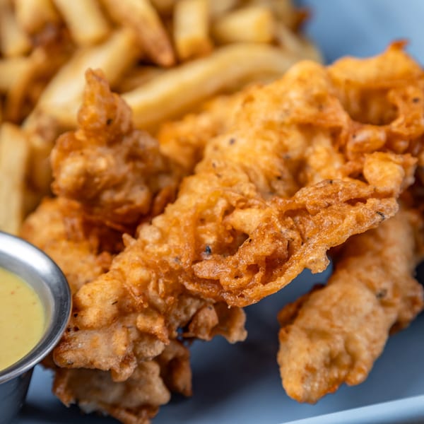 Crispy fried chicken tenders and golden french fries with a side of dipping sauce on a blue plate.