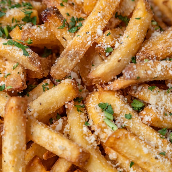 Close-up of golden LSA Burger Co. fries, sprinkled with Parmesan cheese and green herbs.