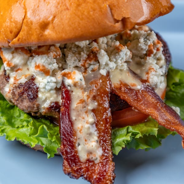 LSA Burger Co. burger with bacon, blue cheese crumbles, and sauce on a bun with lettuce and tomato.