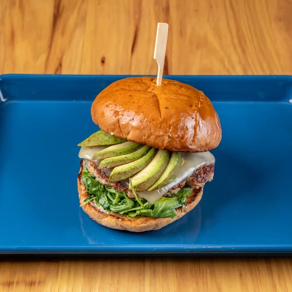 LSA Burger Co. burger with avocado, cheese, and arugula on a blue plate.