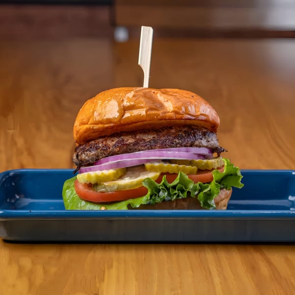 LSA Burger Co. burger with patty, red onion, pickles, tomato, and lettuce on a blue tray.