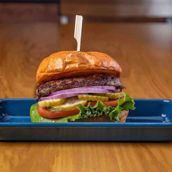LSA Burger Co. burger with patty, red onion, pickles, tomato, and lettuce on a blue tray.